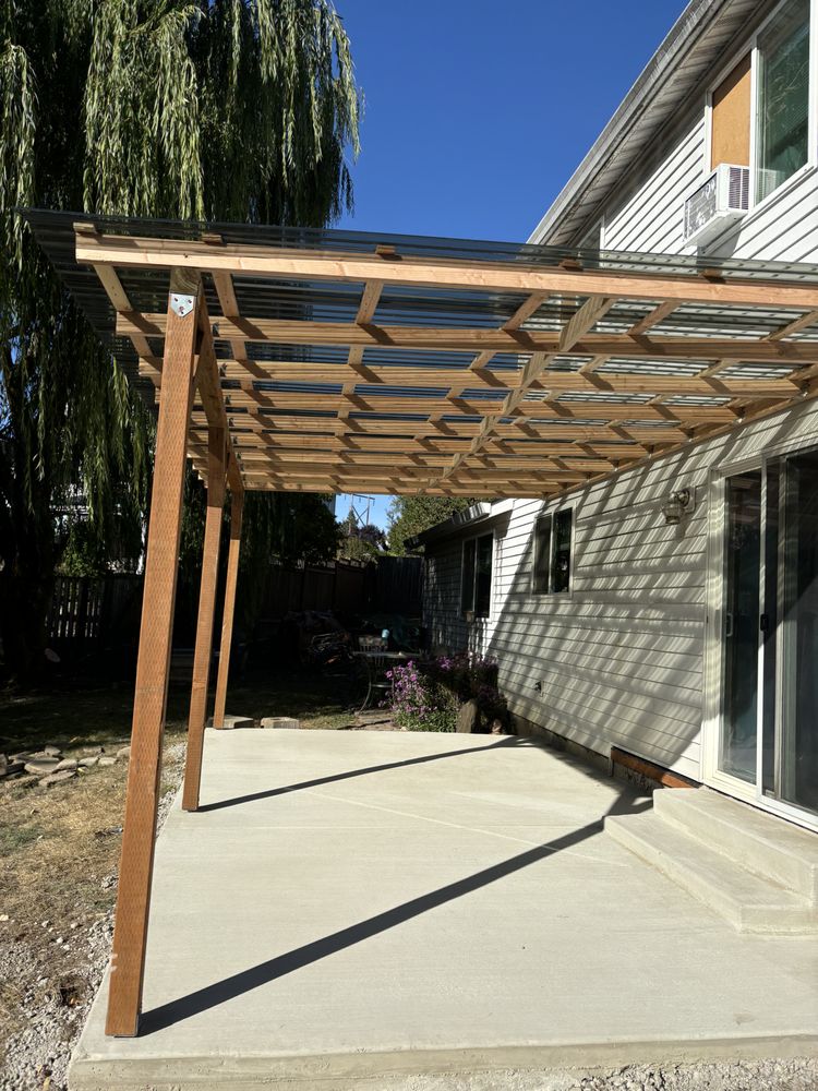 A wooden pergola stands on a patio, providing shade in front of a charming house.