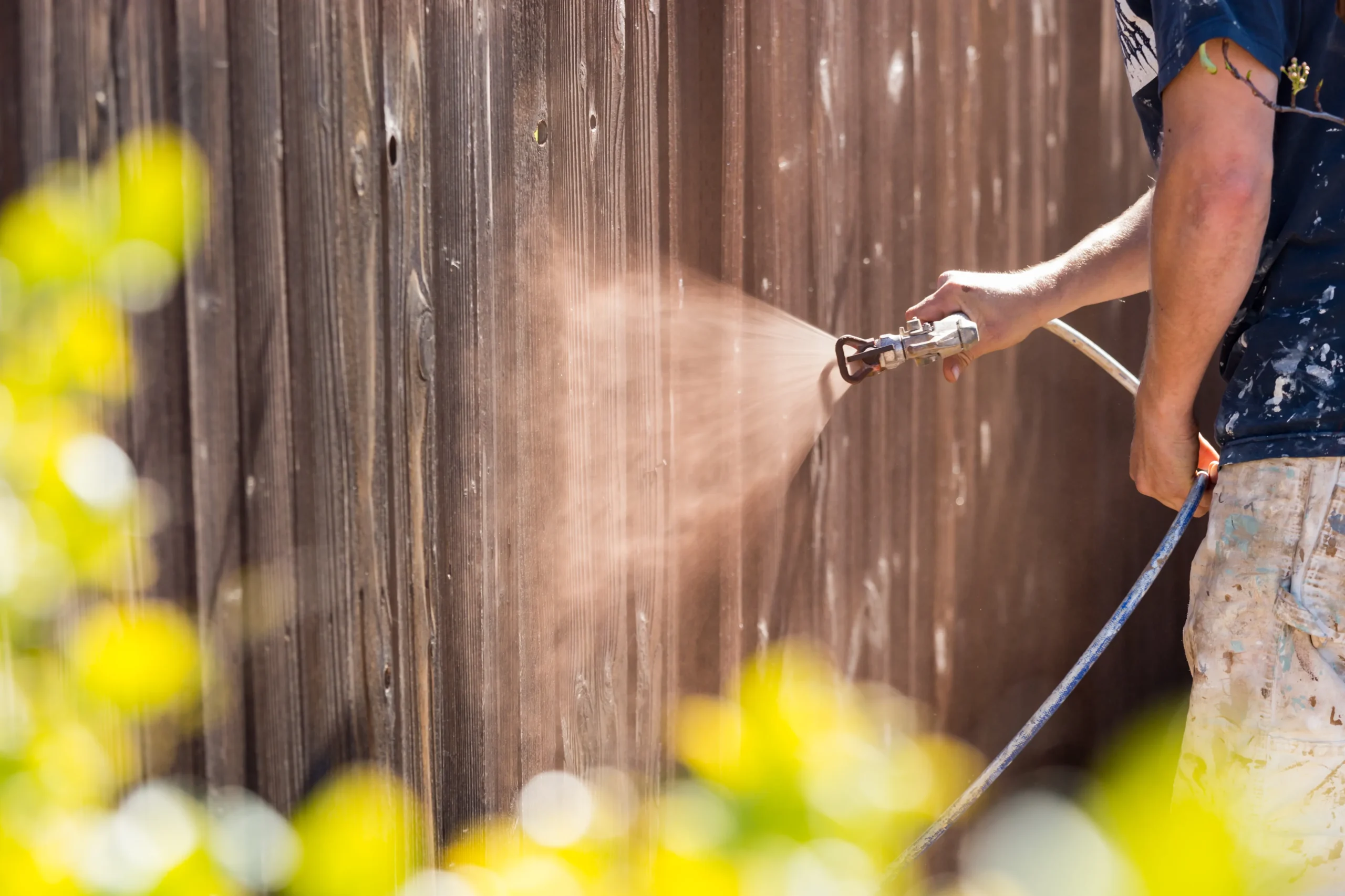  Wood fencing getting a protective stain sprayed for long-lasting durability.